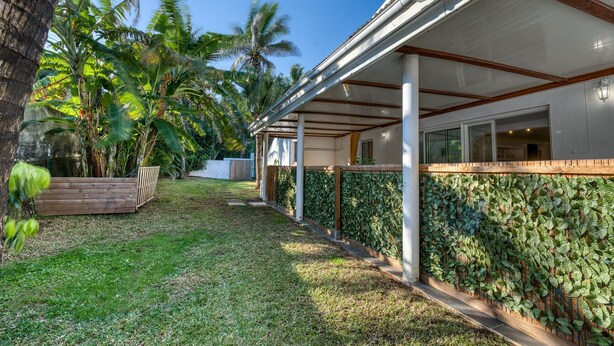 A covered outdoor area with a wooden deck, a wall covered in climbing plants, and a clear blue sky. - La Case Coco - Bananes - Appartement climatisé (Saint Joseph)