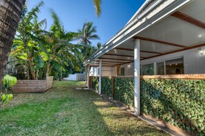 A covered outdoor area with a wooden deck, a wall covered in climbing plants, and a clear blue sky. - La Case Coco - Bananes - Appartement climatisé (Saint Joseph)