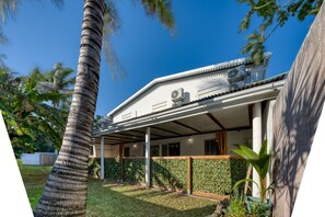 Una casa moderna con un porche cubierto, palmeras y un jardín cuidado.