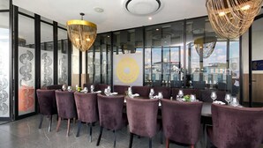 A restaurant with purple velvet chairs, a modern chandelier, and a glass wall with a city view. - Effortless Luxury in Rosebank (Johannesburg)