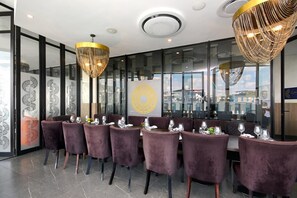 A restaurant with purple velvet chairs, a modern chandelier, and a glass wall with a city view. - Effortless Luxury in Rosebank (Johannesburg)