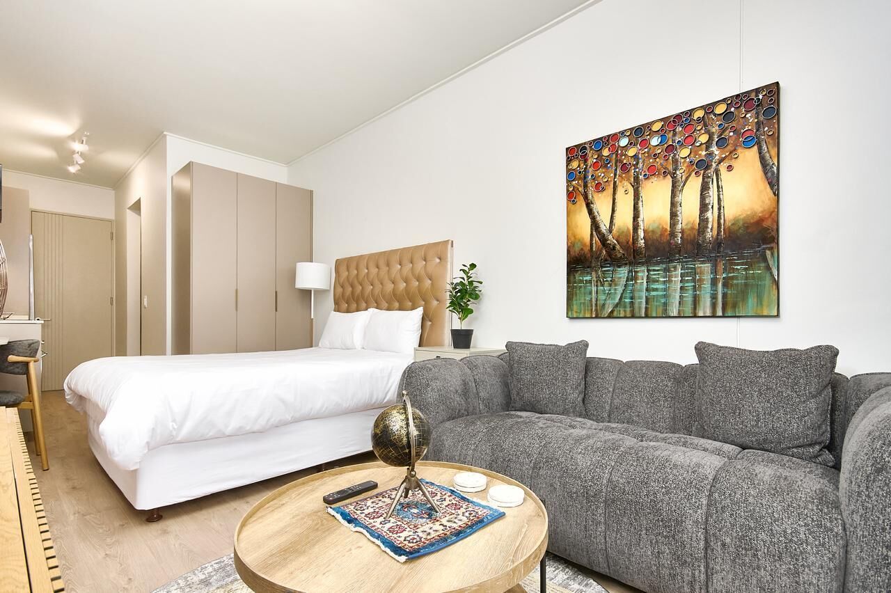 A modern bedroom with a bed, a grey sofa, a round coffee table, and a painting on the wall.