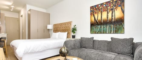 A modern bedroom with a bed, a grey sofa, a round coffee table, and a painting on the wall.