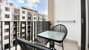 A balcony with a table and chairs, overlooking a building with multiple balconies and windows. - Effortless Luxury in Rosebank (Johannesburg)