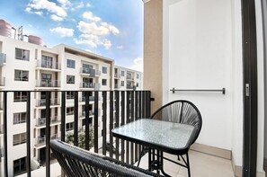 A balcony with a table and chairs, overlooking a building with multiple balconies and windows. - Effortless Luxury in Rosebank (Johannesburg)
