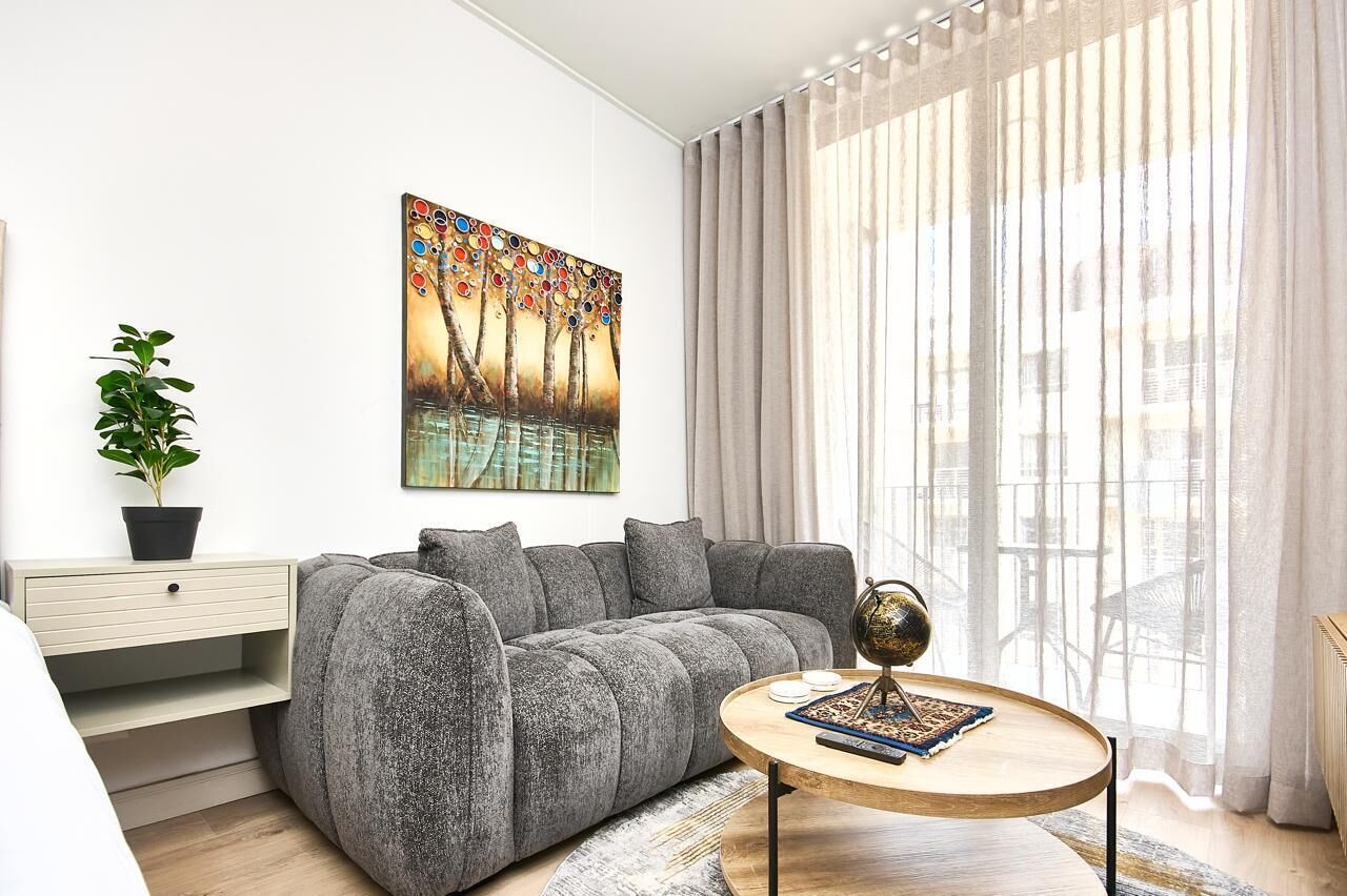 A modern living room with a grey sofa, a round coffee table, a painting on the wall, and a plant on a side table.