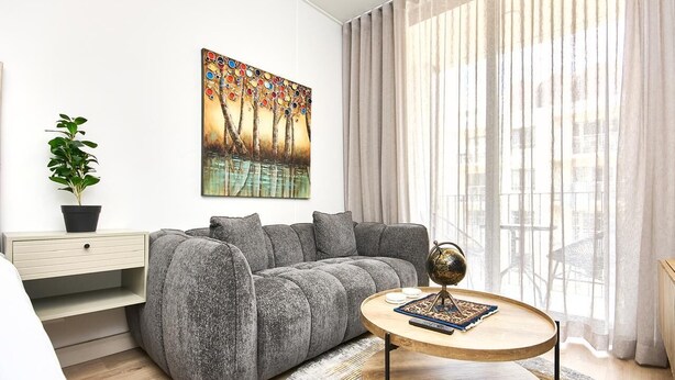 A modern living room with a grey sofa, a round coffee table, a painting on the wall, and a plant on a side table. - Effortless Luxury in Rosebank (Johannesburg)