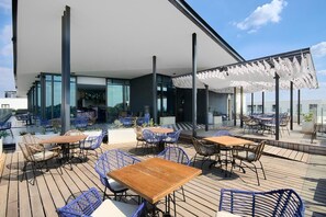An outdoor seating area with tables and chairs, a covered section with umbrellas, and a view of the cityscape. - Effortless Luxury in Rosebank (Johannesburg)