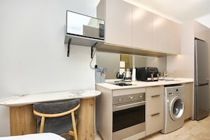 A compact kitchen with a built-in microwave, oven, and washing machine. - Effortless Luxury in Rosebank (Johannesburg)