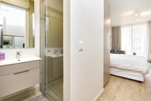 A modern bathroom with a glass shower enclosure, a white sink, and a mirror. - Effortless Luxury in Rosebank (Johannesburg)