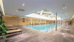 An indoor swimming pool with lounge chairs and a ceiling with a geometric design.