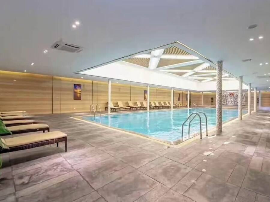 Une piscine intérieure dotée de chaises longues et d’un plafond au motif géométrique.