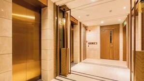 Un hall d’hôtel au design moderne, comprenant un ascenseur central, un comptoir d’accueil et une porte en bois.