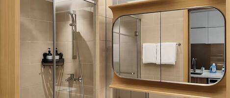 A modern bathroom with a glass-enclosed shower, a large mirror, and a vanity with a sink and toiletries.