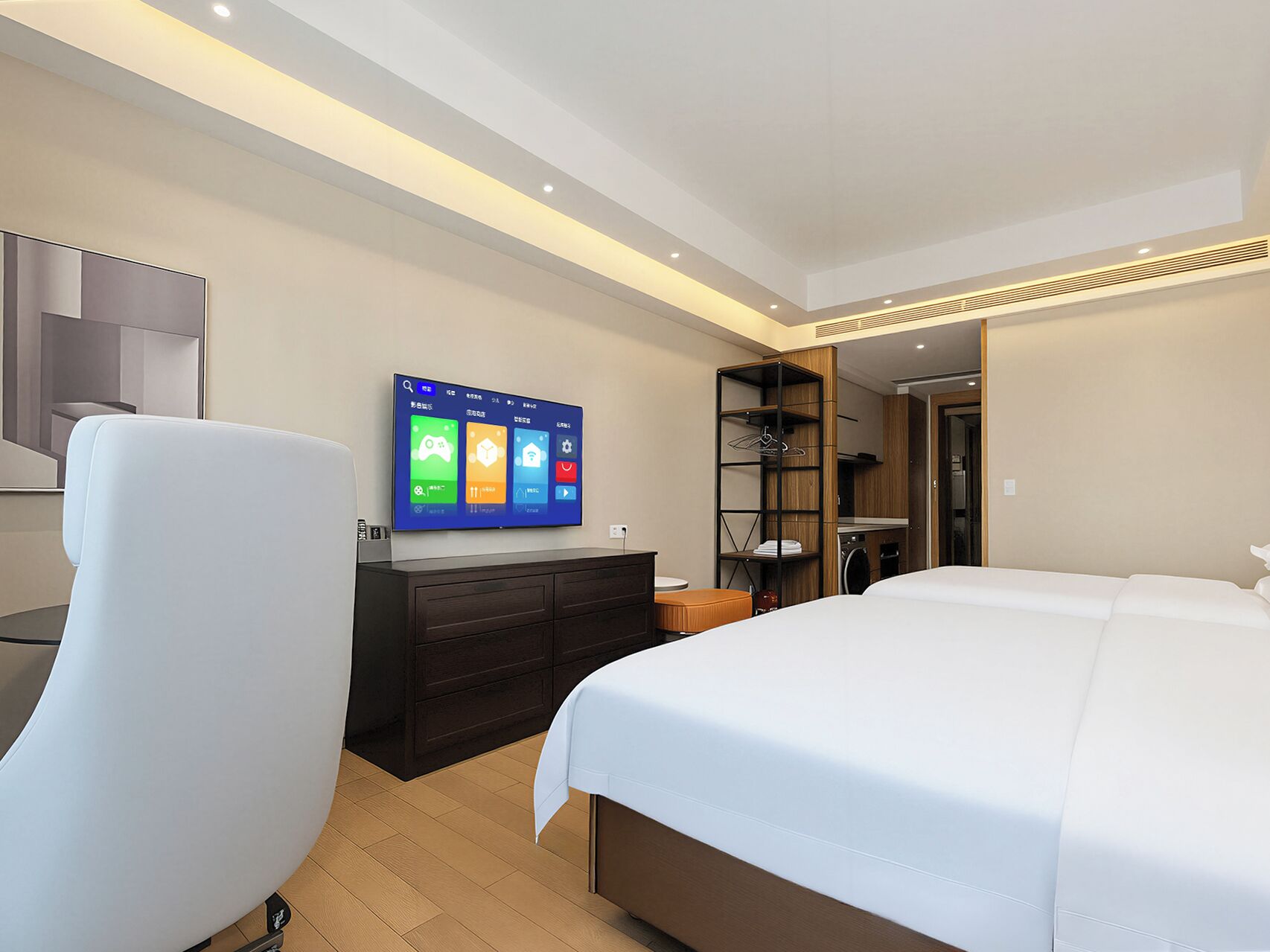 Een moderne hotelkamer met een groot bed, een flatscreen televisie aan de wand, een houten kledingkast en een zithoek met een witte fauteuil.