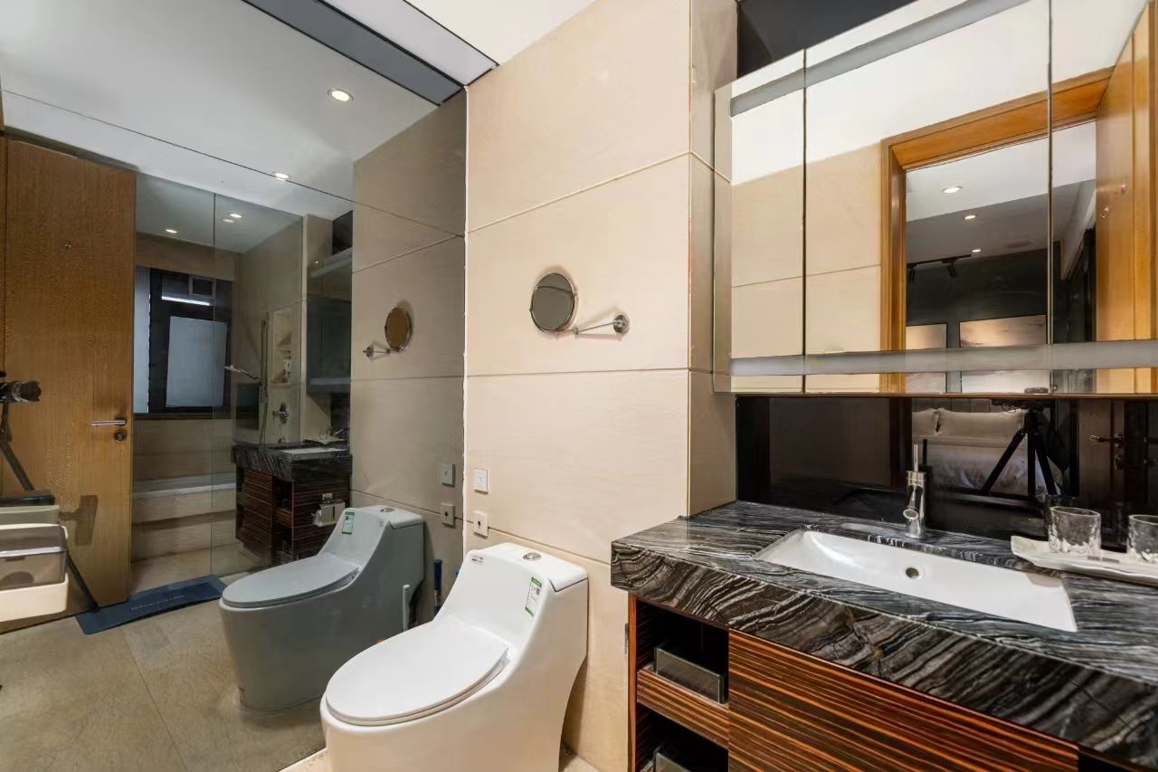 A modern bathroom with a marble sink, two toilets, and a large mirror.