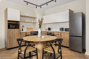 A modern kitchen with a round wooden table, black chairs, and a stainless steel refrigerator. - Park Place, Designer Retreat, Lake Views (Cape Town)