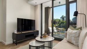 A modern living room with a flat-screen TV, a small coffee table, and a sofa. - Park Place, Designer Retreat, Lake Views (Cape Town)