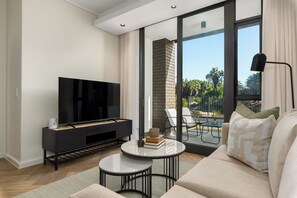 A modern living room with a flat-screen TV, a small coffee table, and a sofa. - Park Place, Designer Retreat, Lake Views (Cape Town)