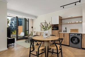 Une cuisine moderne dotée d’un lave-linge encastré, de meubles en bois et d’un coin repas avec une table ronde et des chaises.