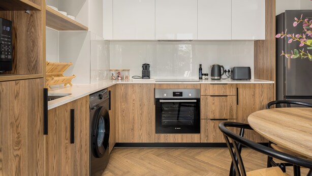 A compact kitchen with wooden cabinetry, a Bosch oven, a washing machine, and a dining area with a table and chairs. - Park Place, Designer Retreat, Lake Views (Cape Town)