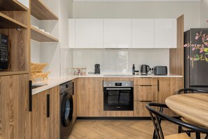 A compact kitchen with wooden cabinetry, a Bosch oven, a washing machine, and a dining area with a table and chairs. - Park Place, Designer Retreat, Lake Views (Cape Town)