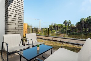 Un balcon avec deux chaises et une table, donnant sur un chantier de construction et sur une zone délimitée par une clôture, où se trouvent des palmiers.