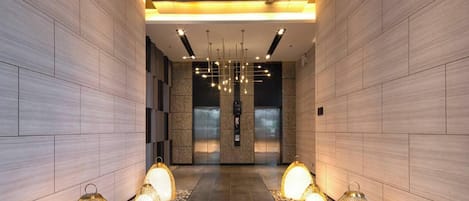 A modern hallway with a central elevator, decorative hanging lights, and a patterned floor.
