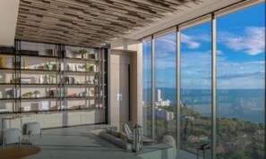 A modern interior with a large bookshelf, a seating area, and a panoramic view through large windows. - Seaview Beach At A Great Price (Pattaya)