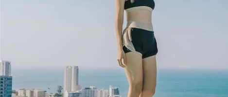 A person standing at the edge of a pool with a cityscape and ocean in the background.