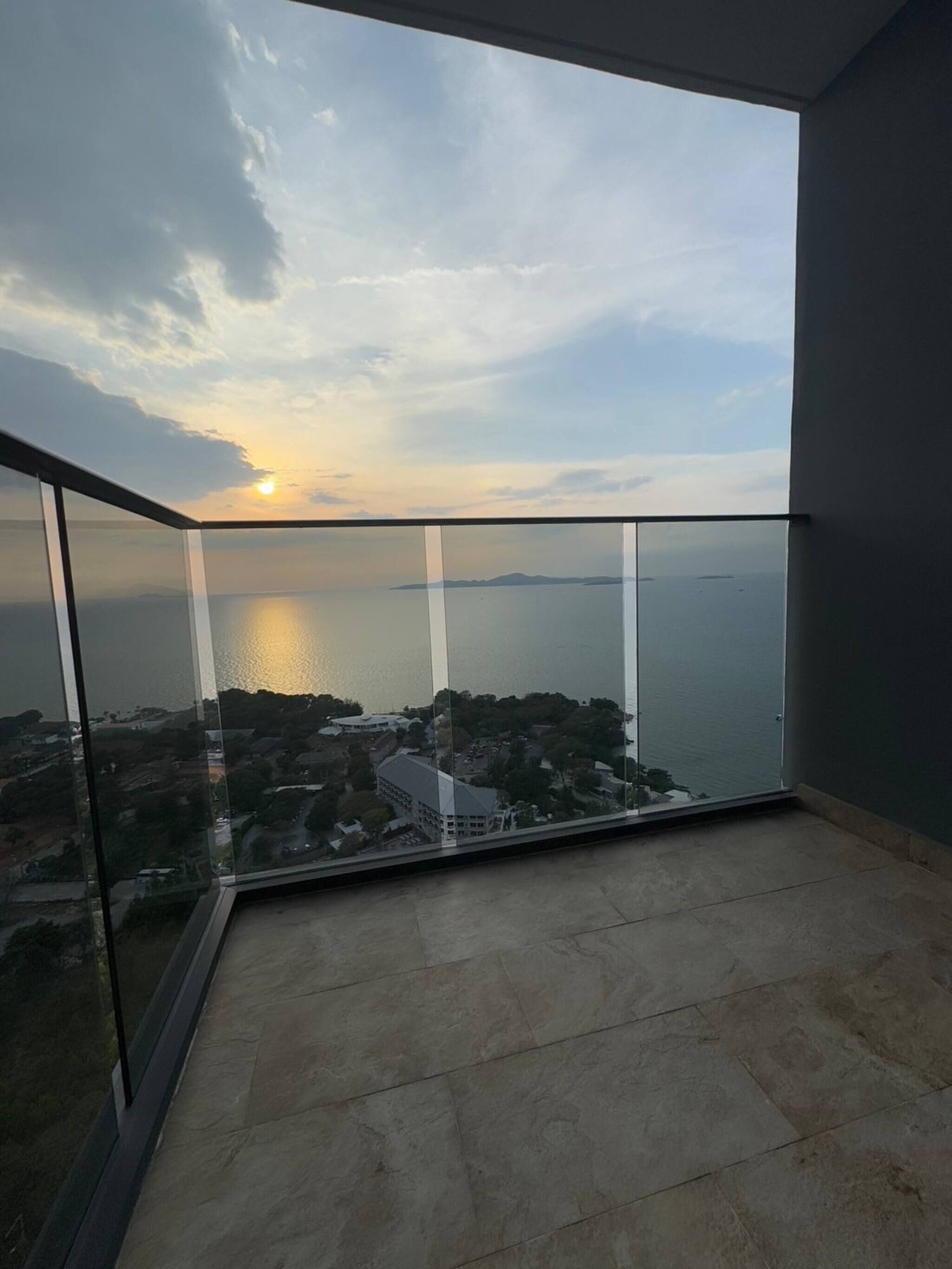 Un balcon offrant une vue sur la mer et la côte lointaine au coucher du soleil.