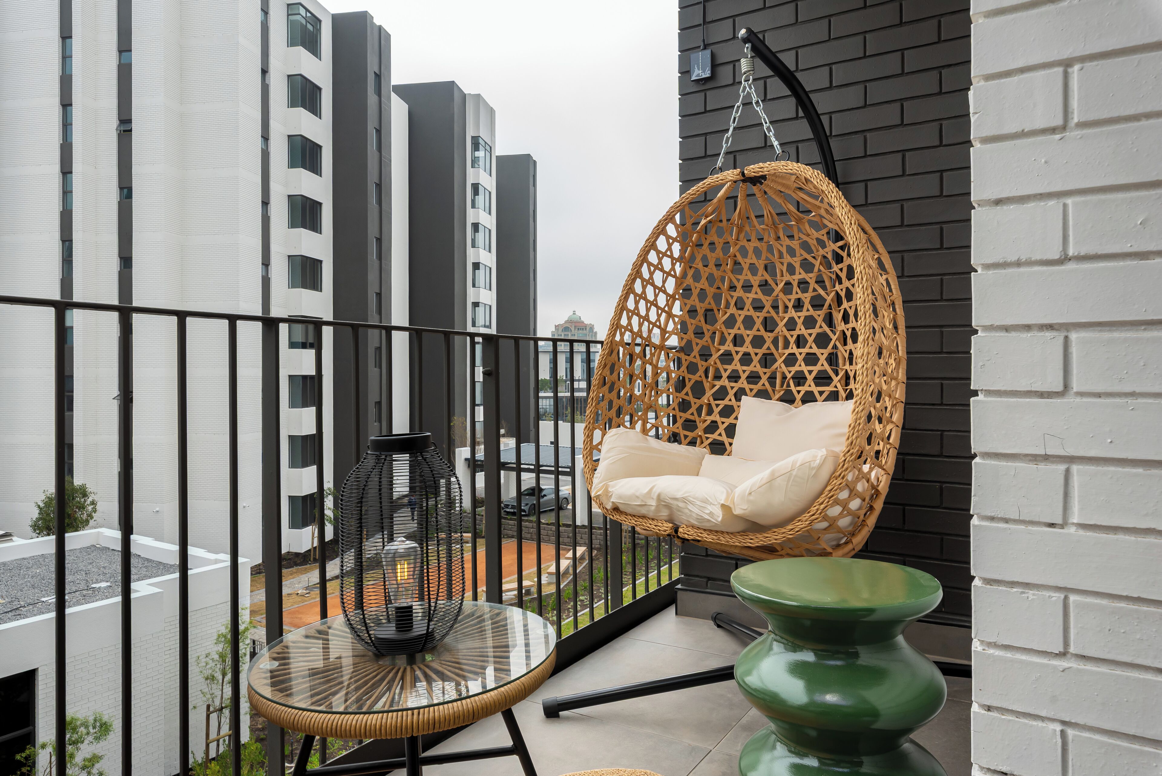 A balcony with a hanging chair, a small table with a lamp, and a green vase.