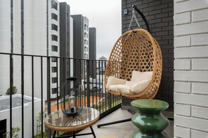 Ein Balkon mit einer Hängematte, einem kleinen Tisch mit einer Lampe und einer grünen Vase.