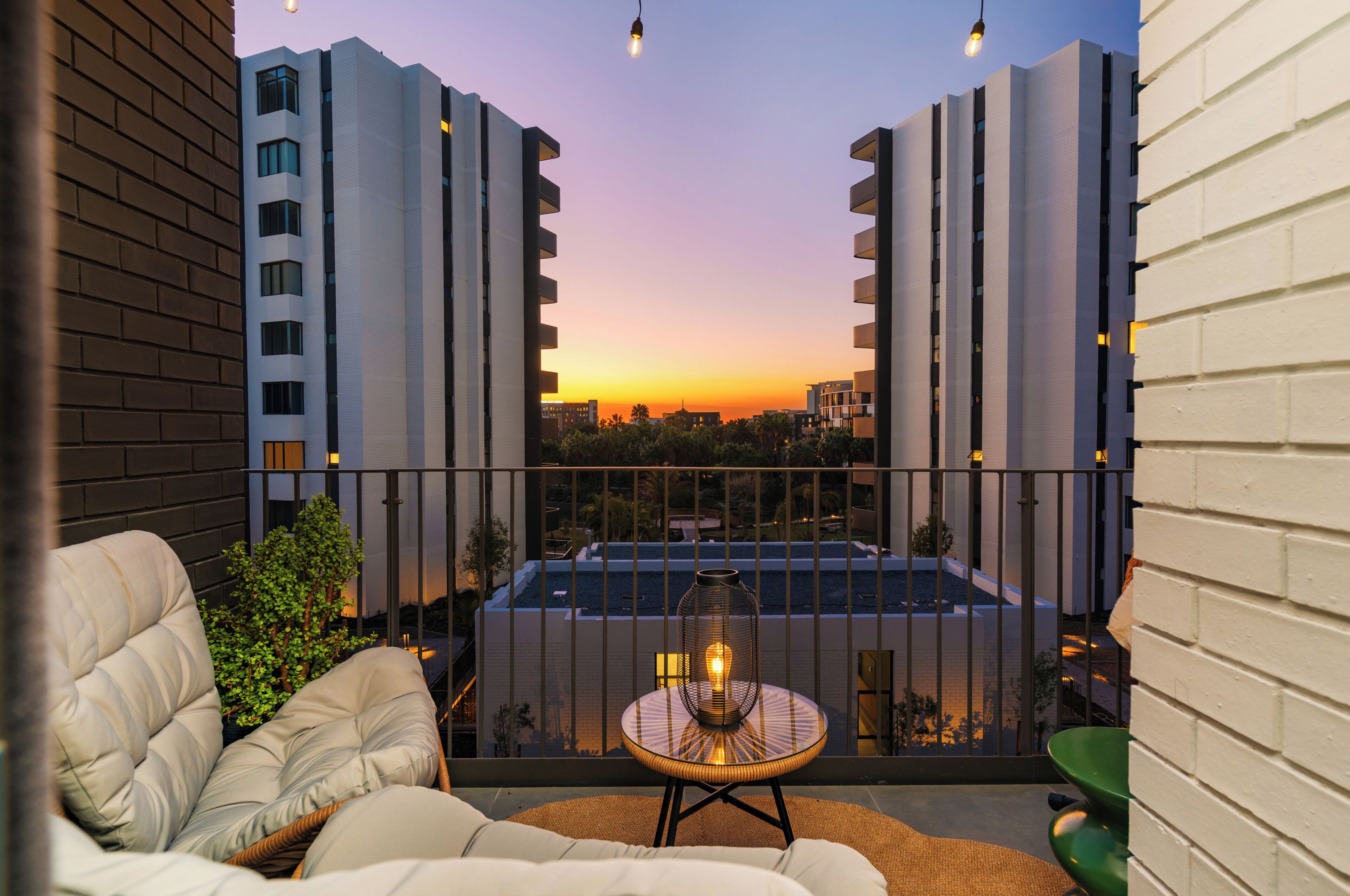 Ein Balkon mit Blick auf einen Sonnenuntergang, ein Schwimmbecken und eine Lounge-Ecke mit Tisch und Stühlen.