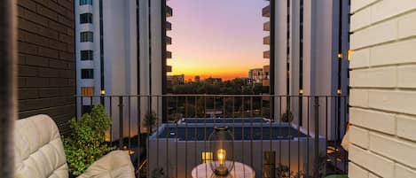 Un balcon avec vue sur le coucher du soleil, une piscine et un espace détente avec une table et des chaises.