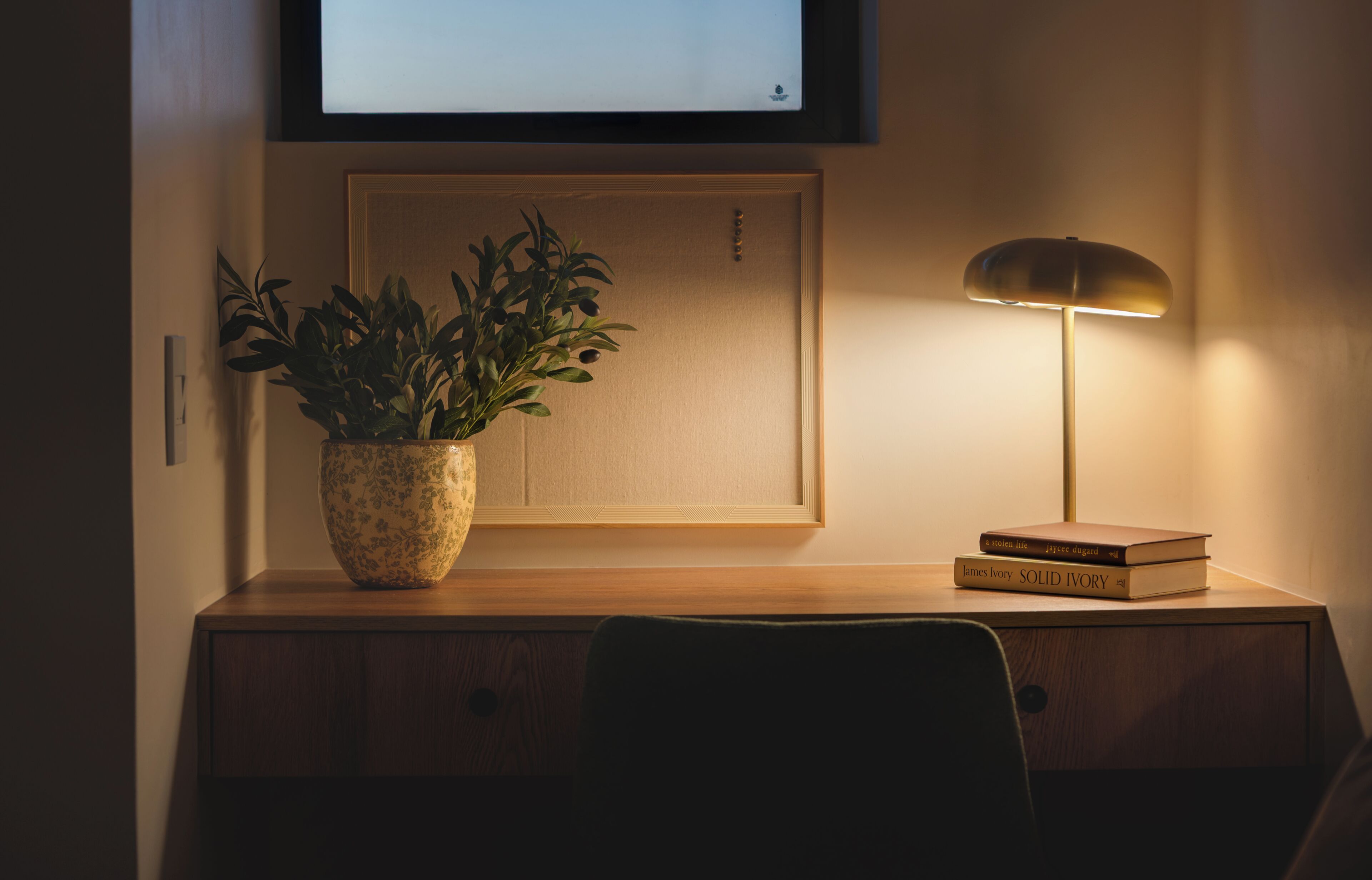 A desk with a potted plant, a lamp, and books.