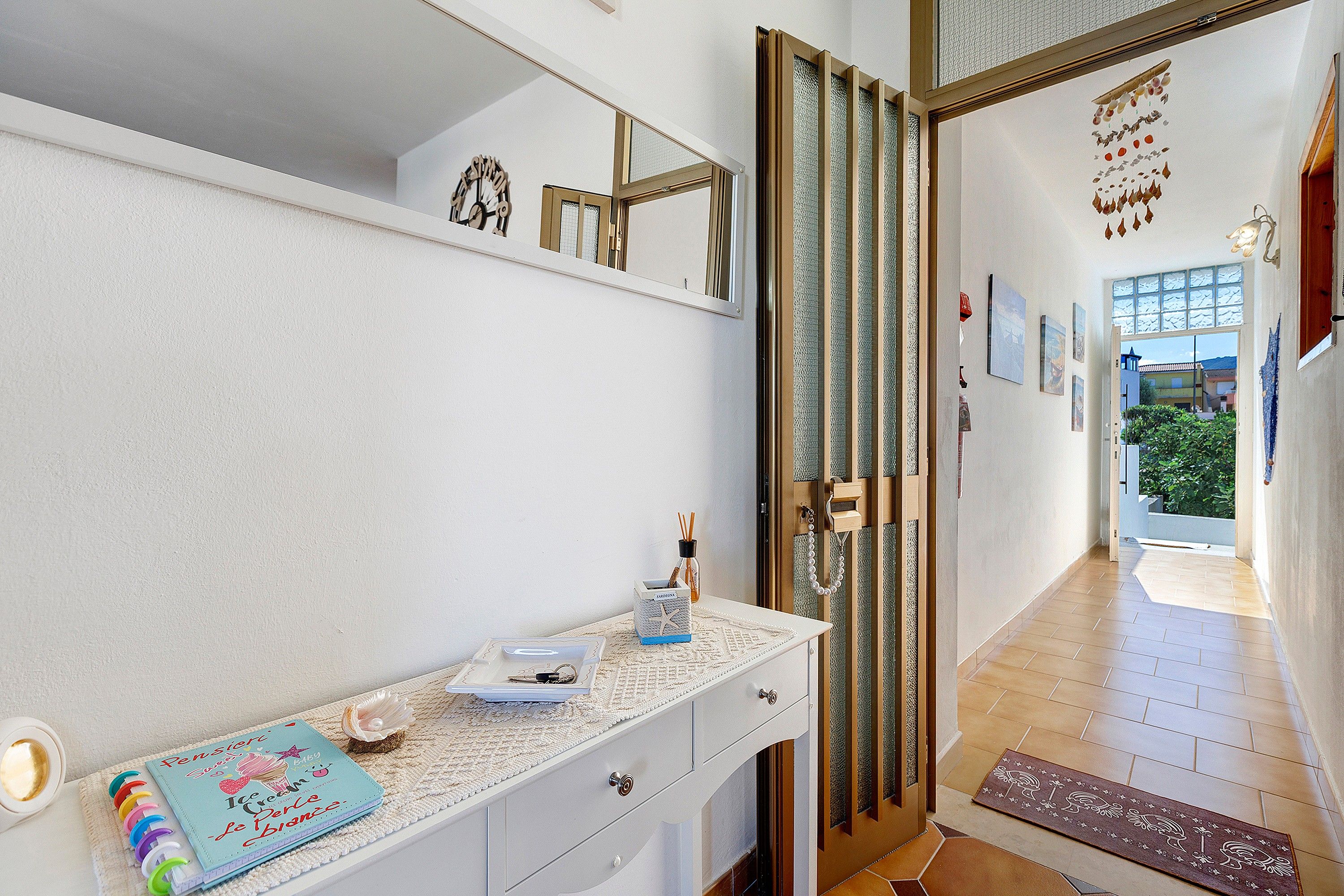 A hallway with a white wall, a door with a decorative glass panel, and a small table with a notebook and a decorative item.