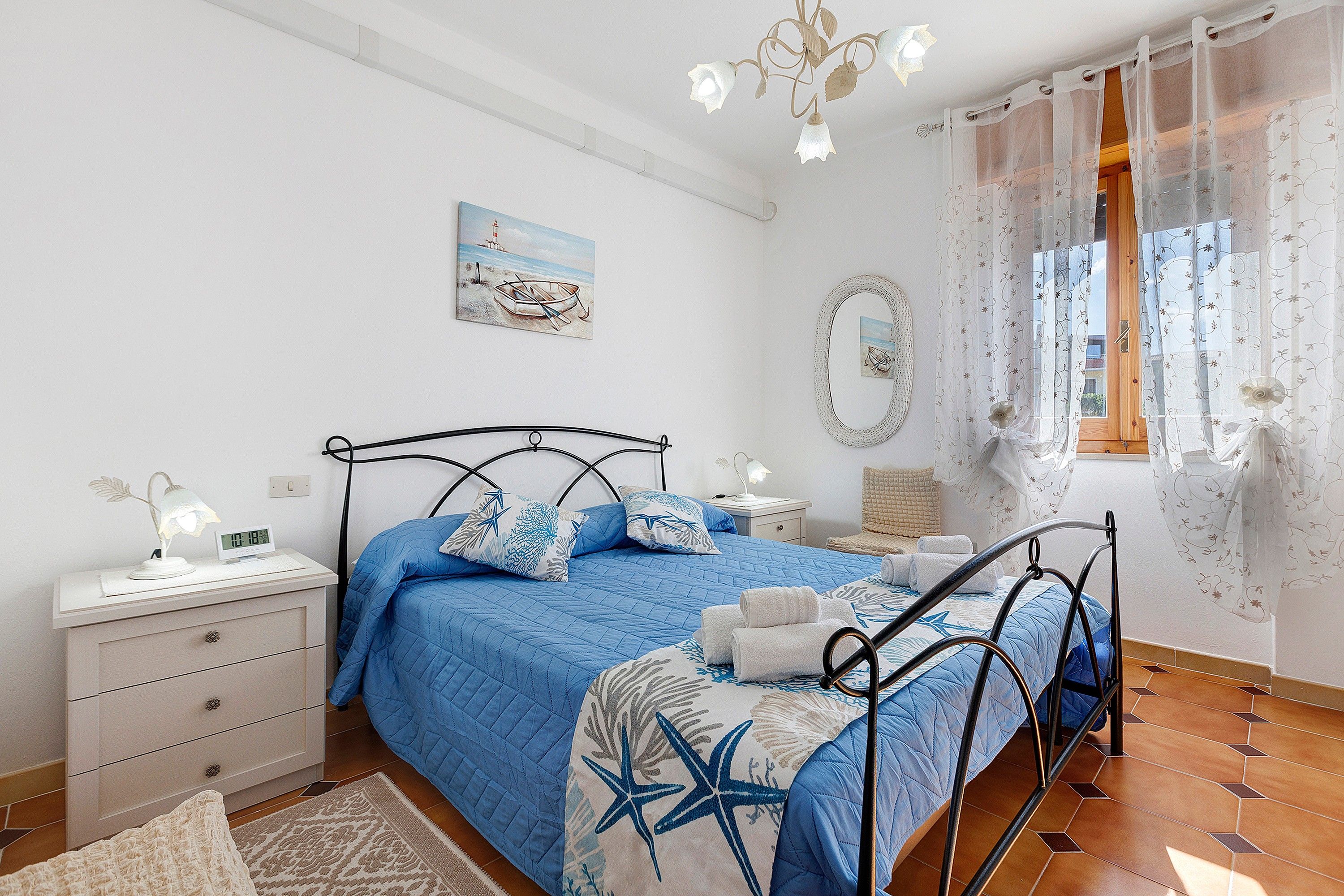 Una camera da letto con un letto, comodini, uno specchio e una finestra con tende.
