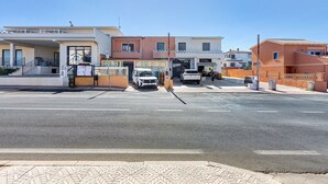 Vista de la calle con un edificio que tiene entrada protegida por una reja y un coche blanco estacionado al frente.