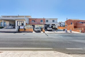 A street view with a building that has a gated entrance and a white car parked in front. - Holiday Home 'La Perla Bianca' with Sea View, Balcony, and Air Conditioning (Lu Bagnu)