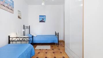 A bedroom with two beds, a small table, a nightstand, a poster on the wall, and a tiled floor.