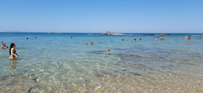 Escena de platja amb aigua cristal·lina i gent nedant.