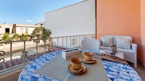 Un balcón con una mesa para dos, un sofá de mimbre blanco y vistas a la calle.