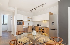 Eine moderne Küche mit einem Glastisch, Holzstühlen, einem Edelstahlkühlschrank und eingebauten Geräten.