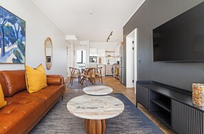 Ein modernes Wohnzimmer mit einer Ledersofa, zwei runden Couchtischen, einem Flachbildfernseher und einer Küche im Hintergrund.
