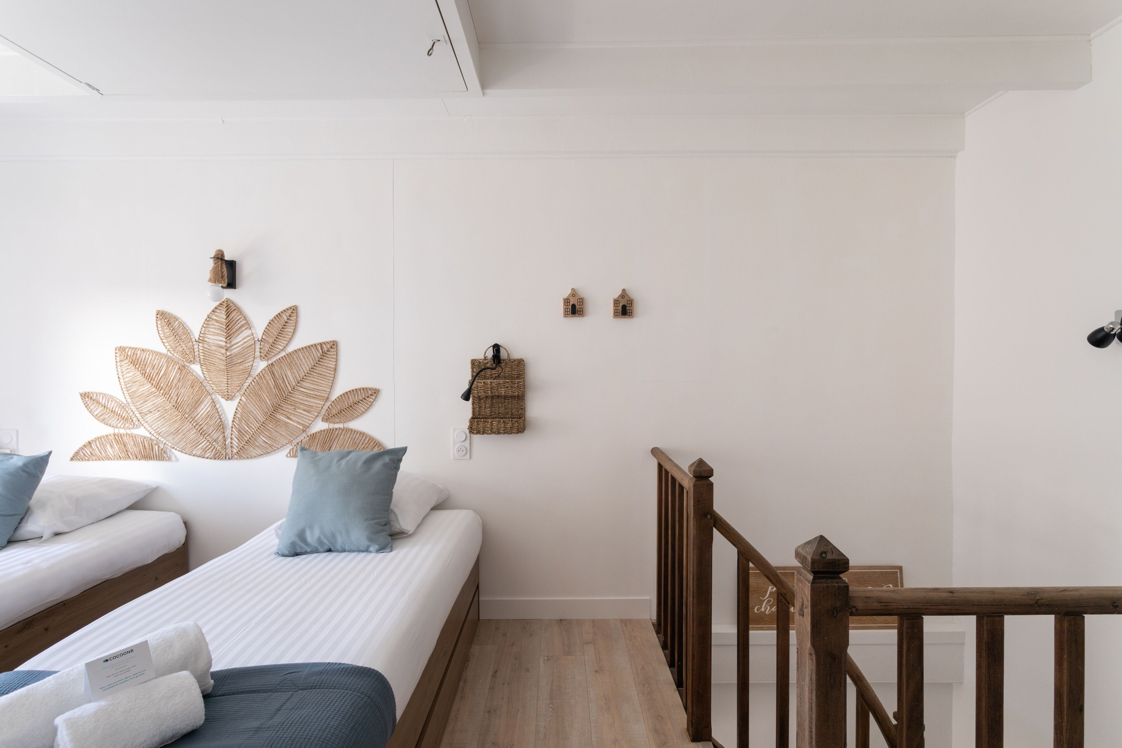 Un dormitorio con dos camas, cabeceros de madera, una lámpara fijada a la pared y un pequeño estante de madera.