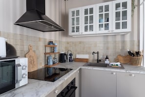 A modern kitchen with a built-in oven, a range hood, and white cabinets with glass doors. - Rose Des Sables - Jolie maison en pierre rénovée (Dinard)