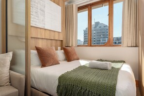 A hotel room with a bed, a view of buildings, and a window with curtains. - Charlie and the Chairman | Modern CBD Retreat (Cape Town)