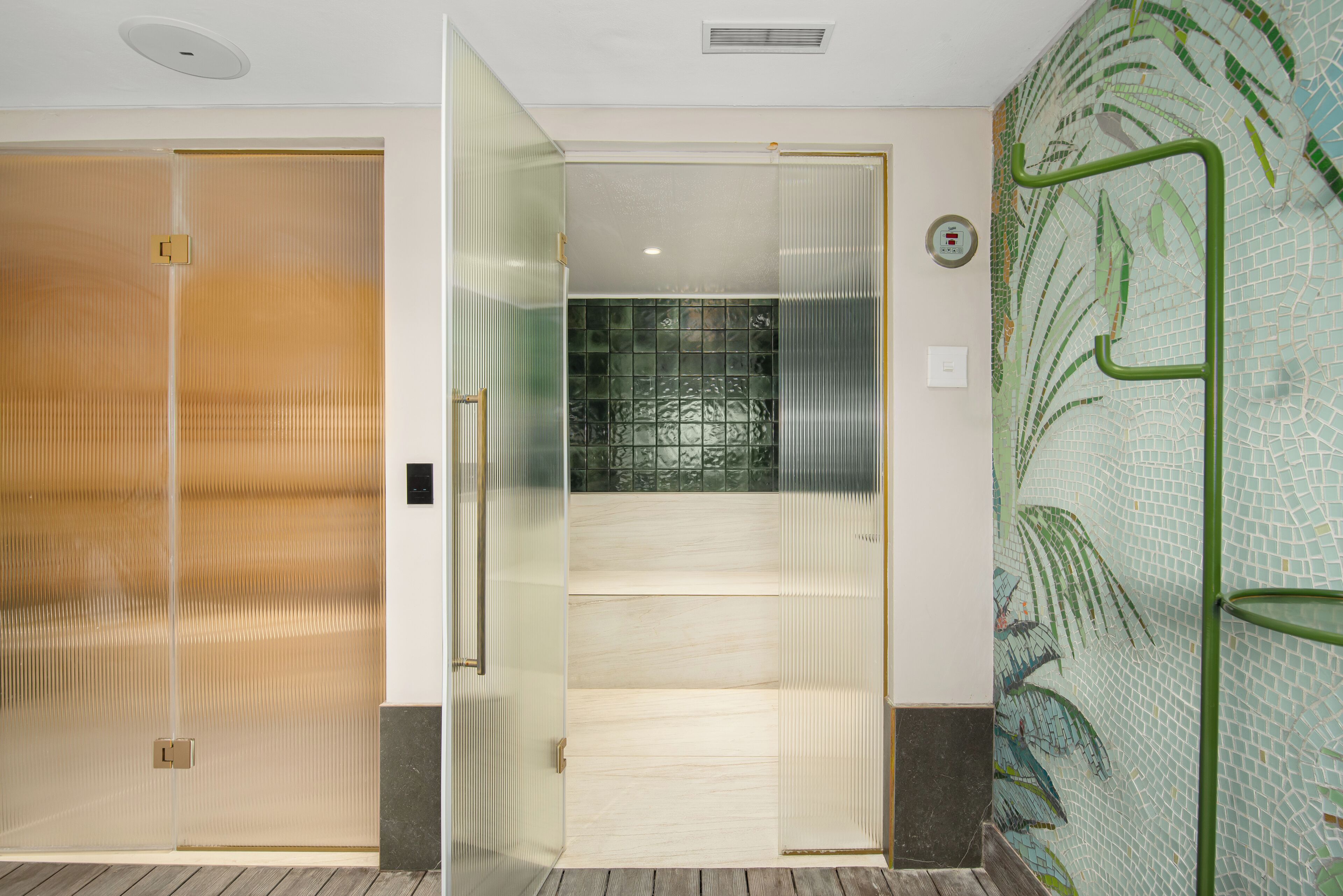 A hotel room with a sliding door, a tiled shower area, and a green metal handrail.