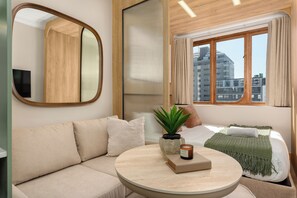A modern hotel room with a sofa, a round table, a potted plant, a candle, and a view of the city through a window. - Charlie and the Chairman | Modern CBD Retreat (Cape Town)
